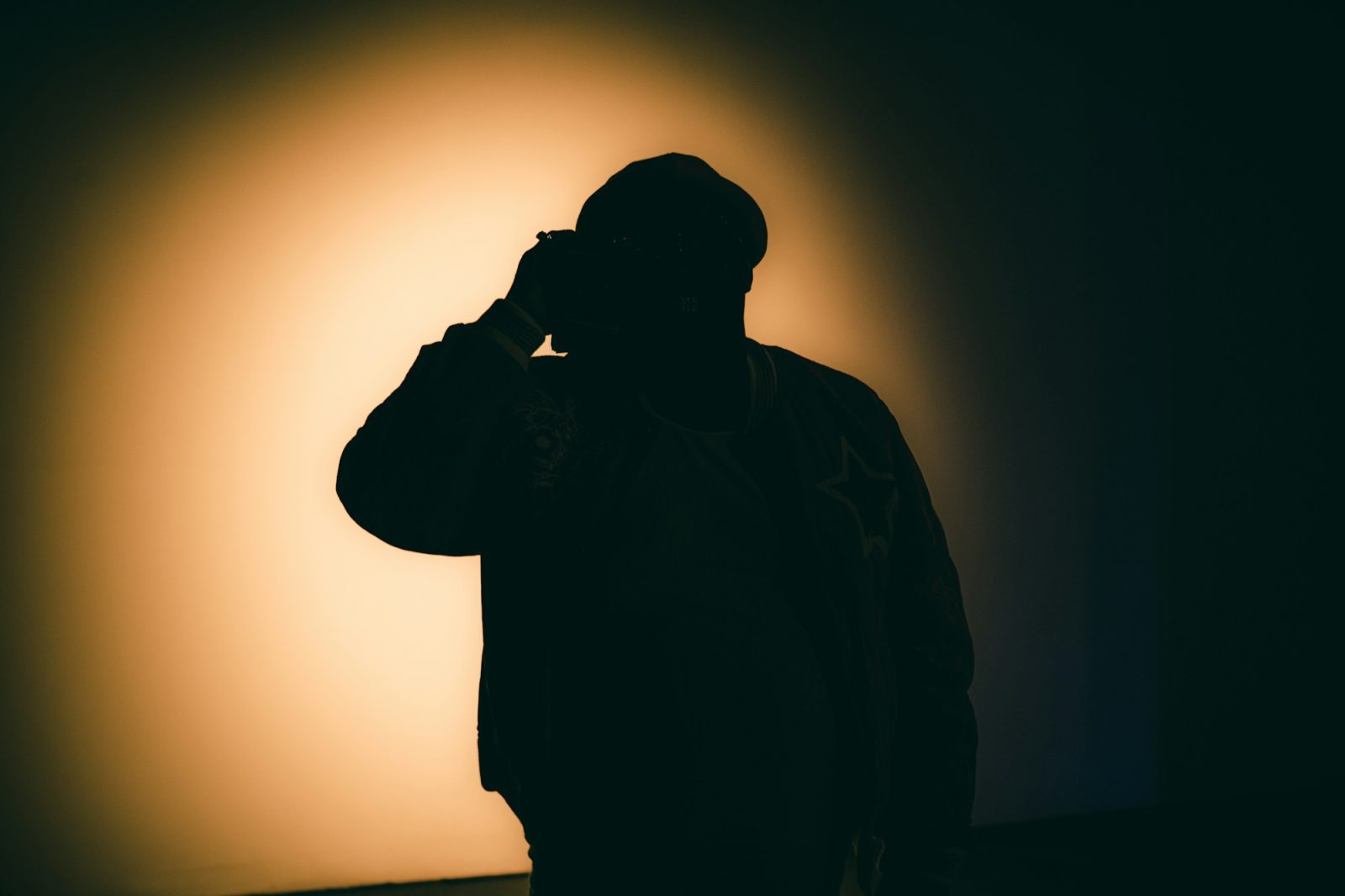 Silhouet van een persoon met pet die in een donkere ruimte een telefoon aan het oor houdt