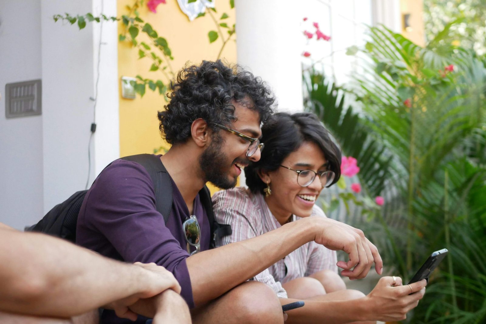 Een man en een vrouw met brillen lachen hardop terwijl ze samen naar een smartphone kijken