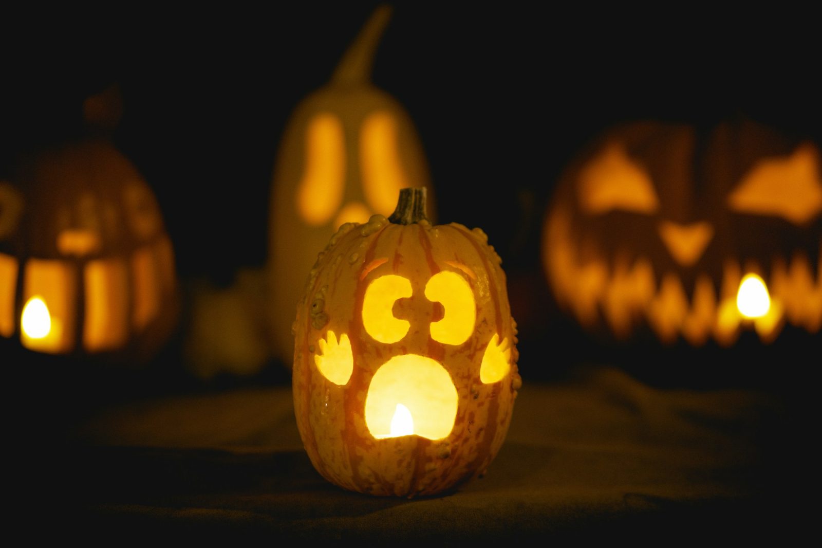Een kleine uitgeholde pompoen met een geschrokken gezicht, met daarachter verlichte halloweenpompoenen in het donker