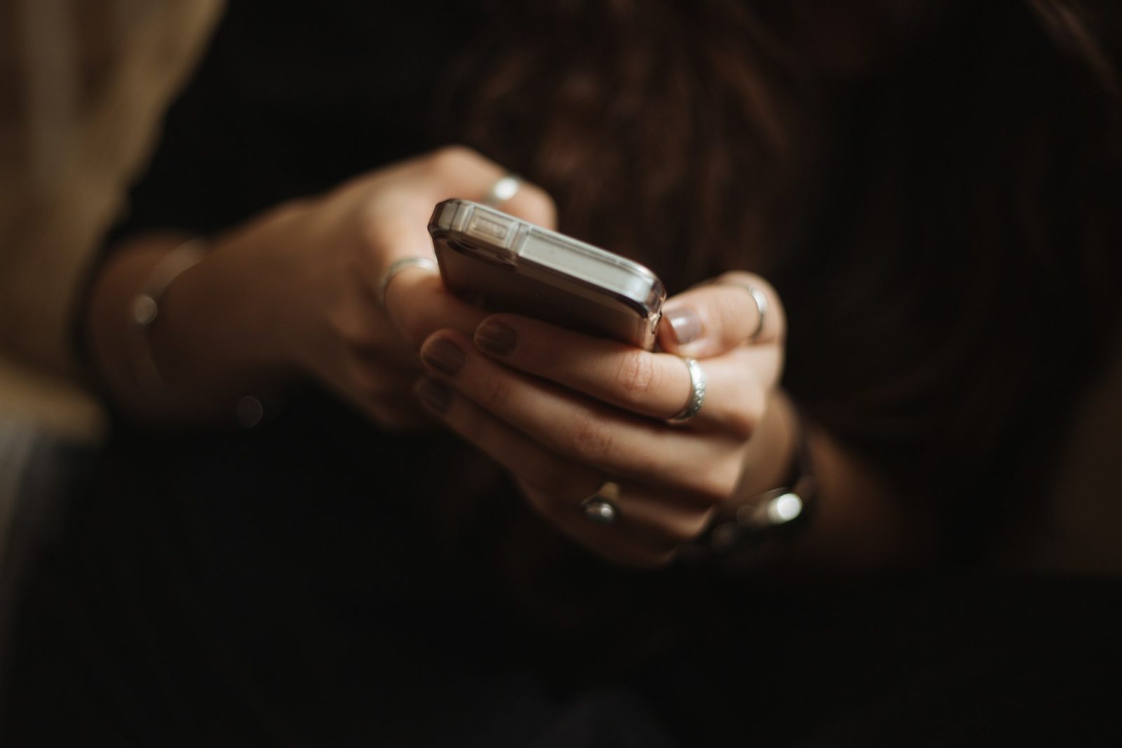 Twee handen met ringen houden een smartphone vast en typen een bericht, tegen een donkere achtergrond