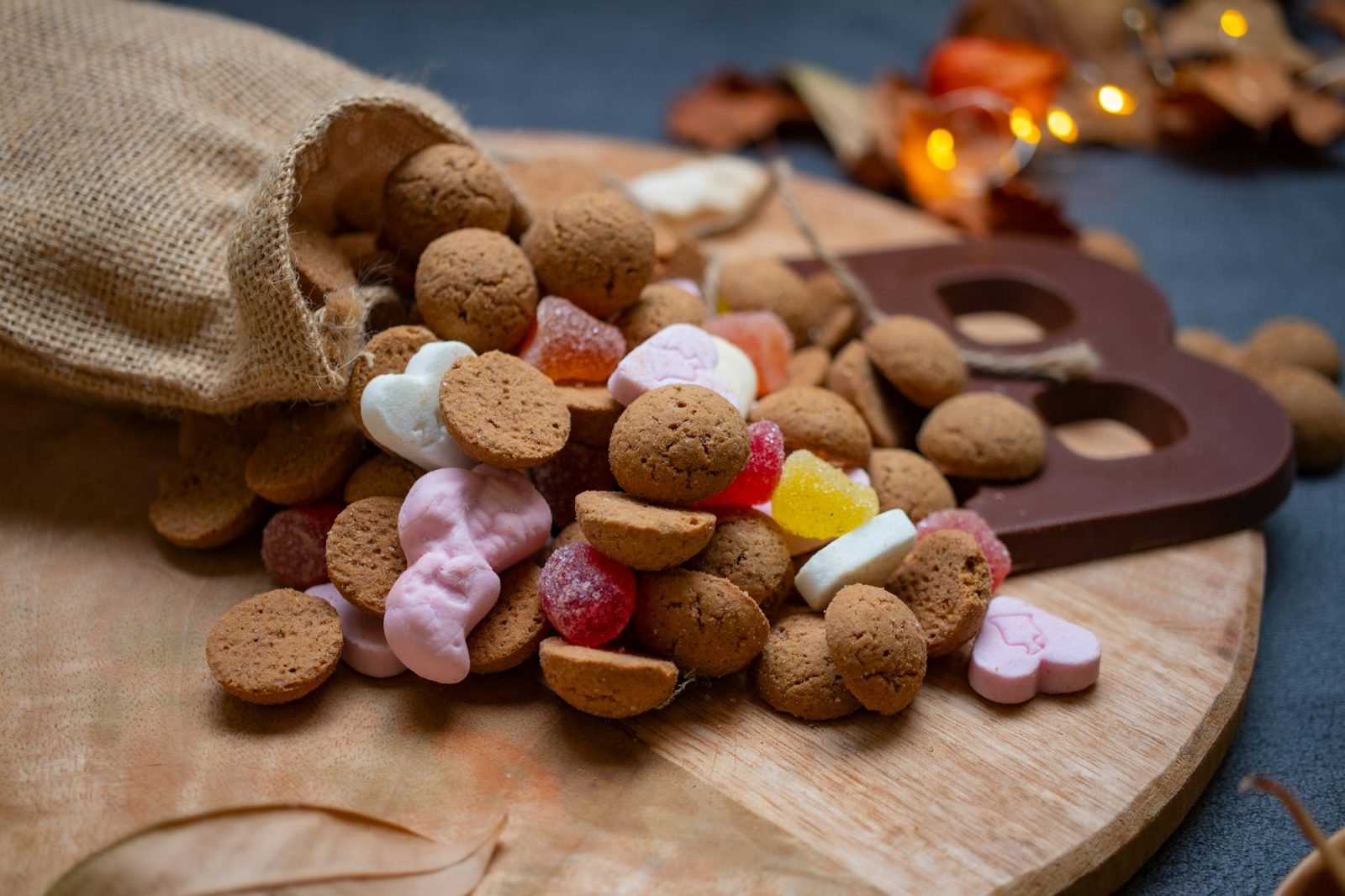Pepernoten en schuimpjes rollen uit een jute zakje naast een chocoladeletter op een houten plank
